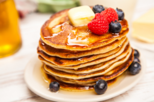 A photo of a stack of pancakes topped with berries, butter and syrup on a white plate.