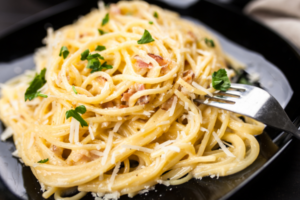 A photo of a black plate of spaghetti carbonara with a fork sticking out of the pasta.