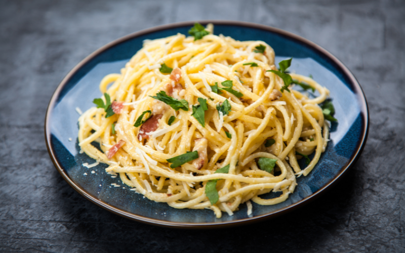 A photo of spaghetti carbonara topped with herbs sitting on a dark blue plate.