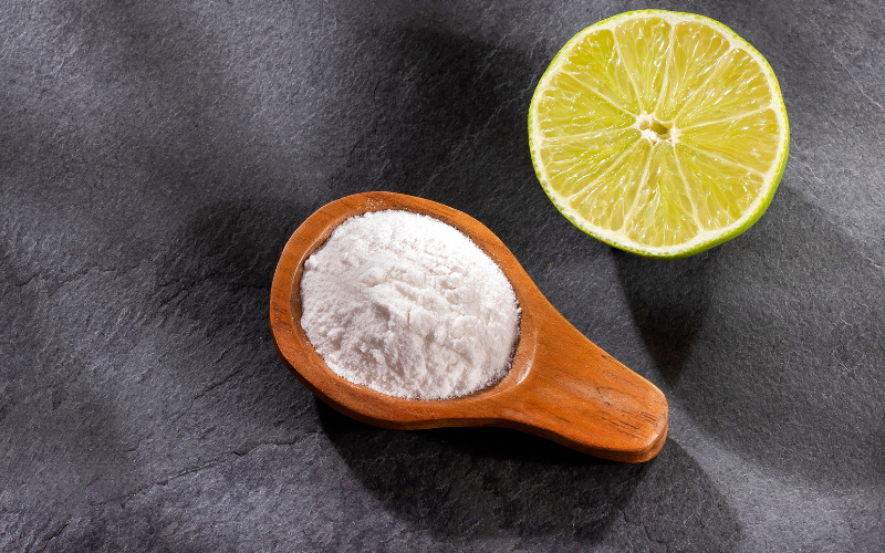 A photo of a spoon holding lemon juice powder. Next to the spoon in half a lemon.