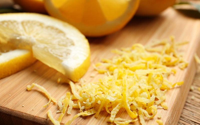 A photo of lemons cut up on a wooden cutting board. Next to the lemons is a pile of lemon peels.