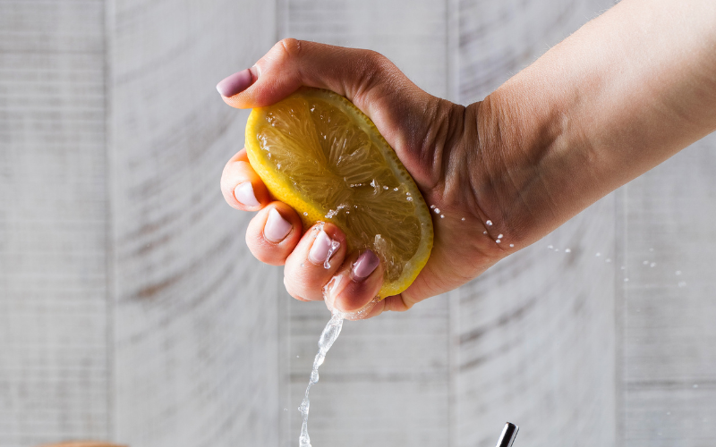 A photo of someone squeezing the juice out of a lemon. The lemon juice is spraying everywhere.