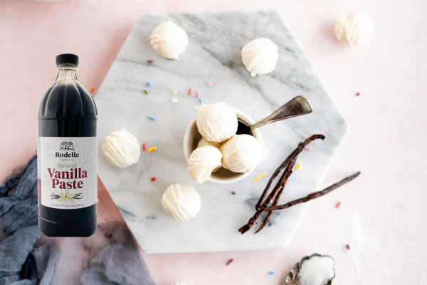 A picture of a bowl of vanilla ice cream on a hexagon marble board. A big bottle of Rodelle ADM vanilla paste is sitting next to the bowl.