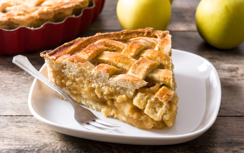 A slice of apple pie, on a white plate, with a fork beside it