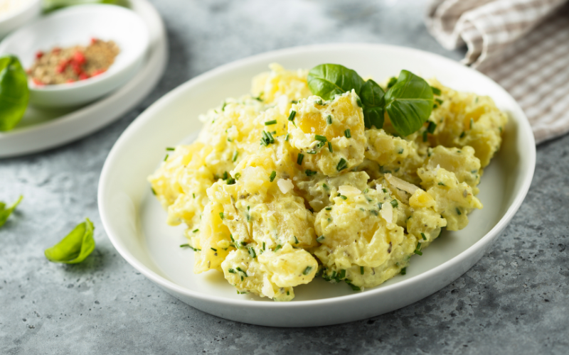 Classic potato salad, featured in a white plate on a gray tabletop