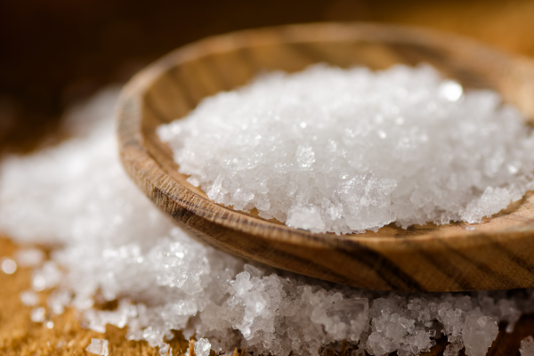 A picture of sea salt on a spoon sitting on more sea salt on a wooden table.