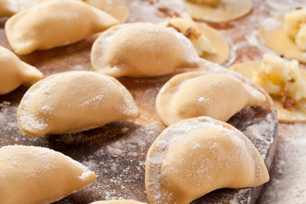 A photo of potato dumplings sprinkled with flour sitting on a wooden cutting board.