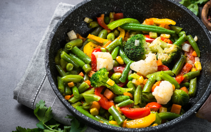 A photo of vegetable stir fry in a frying pan on top of a grey cloth.