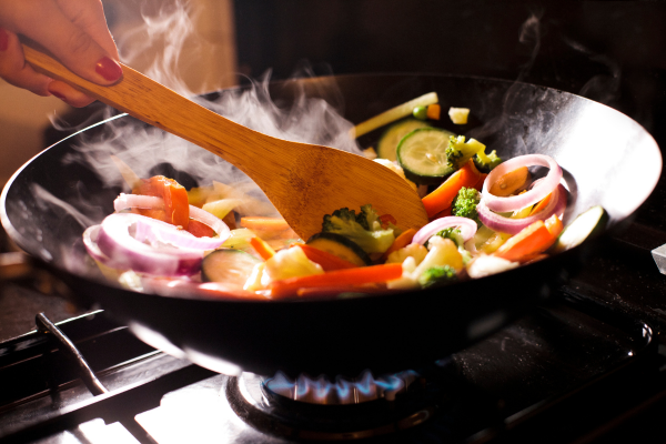 A photo of someone stirring vegetable stir fry with a wooden spoon on the stove.