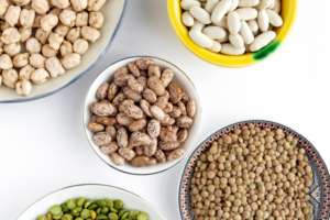 Chickpeas, lentils, and other legumes featured on a white tabletop in their own separate bowls