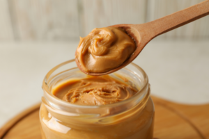 A wooden spoon scooping peanut butter out of a container, for national peanut butter day